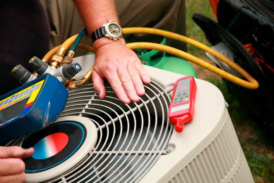 HVAC technician putting hand over outdoor unit while servicing it.