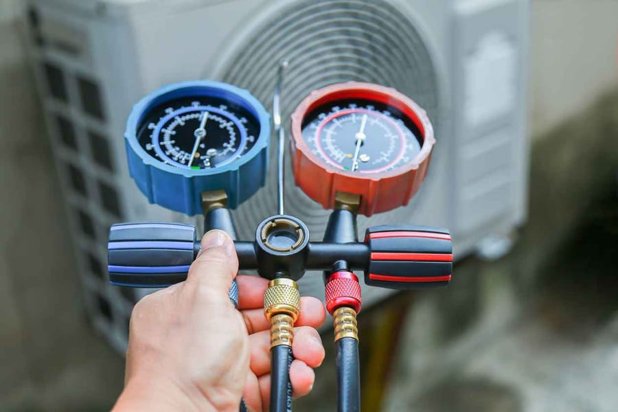 HVAC service technician using gauges to check refrigerant and add refrigerant.